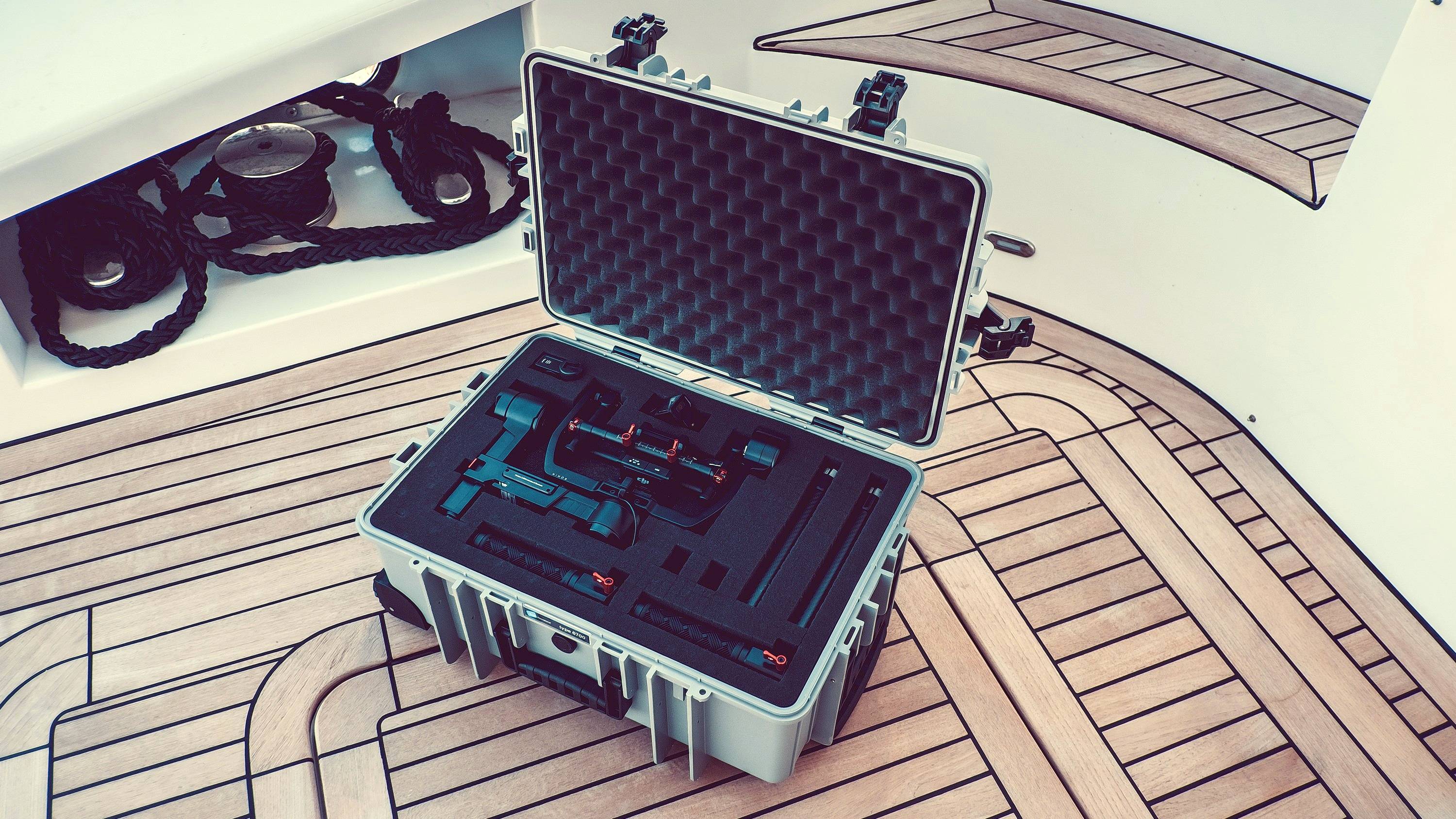 Ein offener Koffer mit Schaumstoffeinlage zeigt präzise Werkzeuge, die auf einem hölzernen Bootsdeck platziert sind.