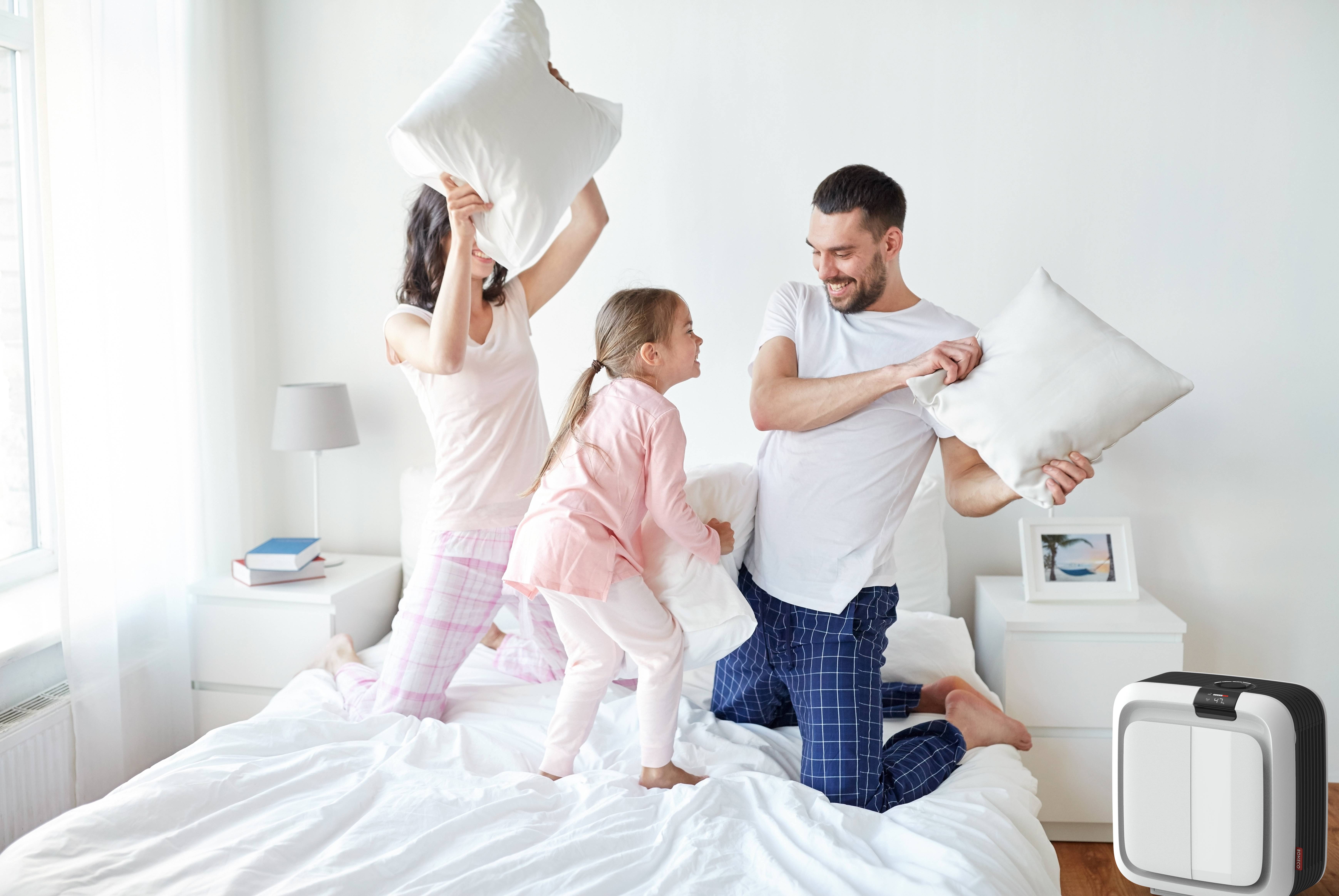 Eine Familie im Schlafanzug hat Spaß bei einer Kissenschlacht auf einem Bett. Ein Mann und zwei Mädchen lachen und spielen.
