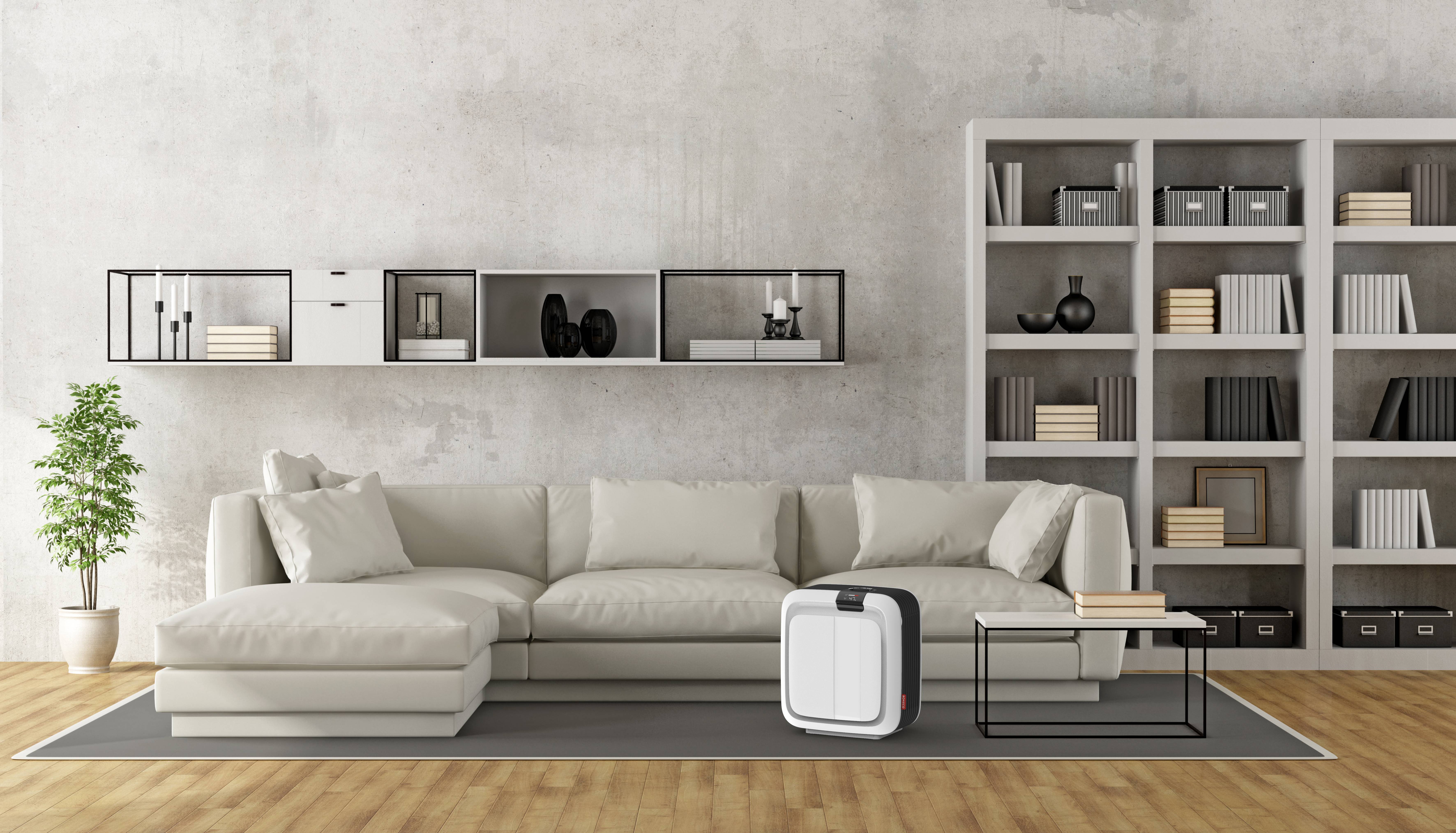 Helles Wohnzimmer mit einem großen, beigen Sofa, dekorativen Wandregalen und einem weißen Luftreiniger auf dem Boden vor dem Sofa.