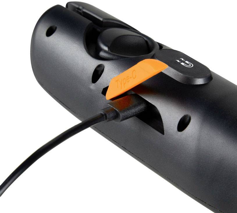 Eine schwarze Fernbedienung mit einem USB-C-Ladekabel angeschlossen, ein orangefarbenes Etikett mit der Aufschrift 'Type-C' ist sichtbar.