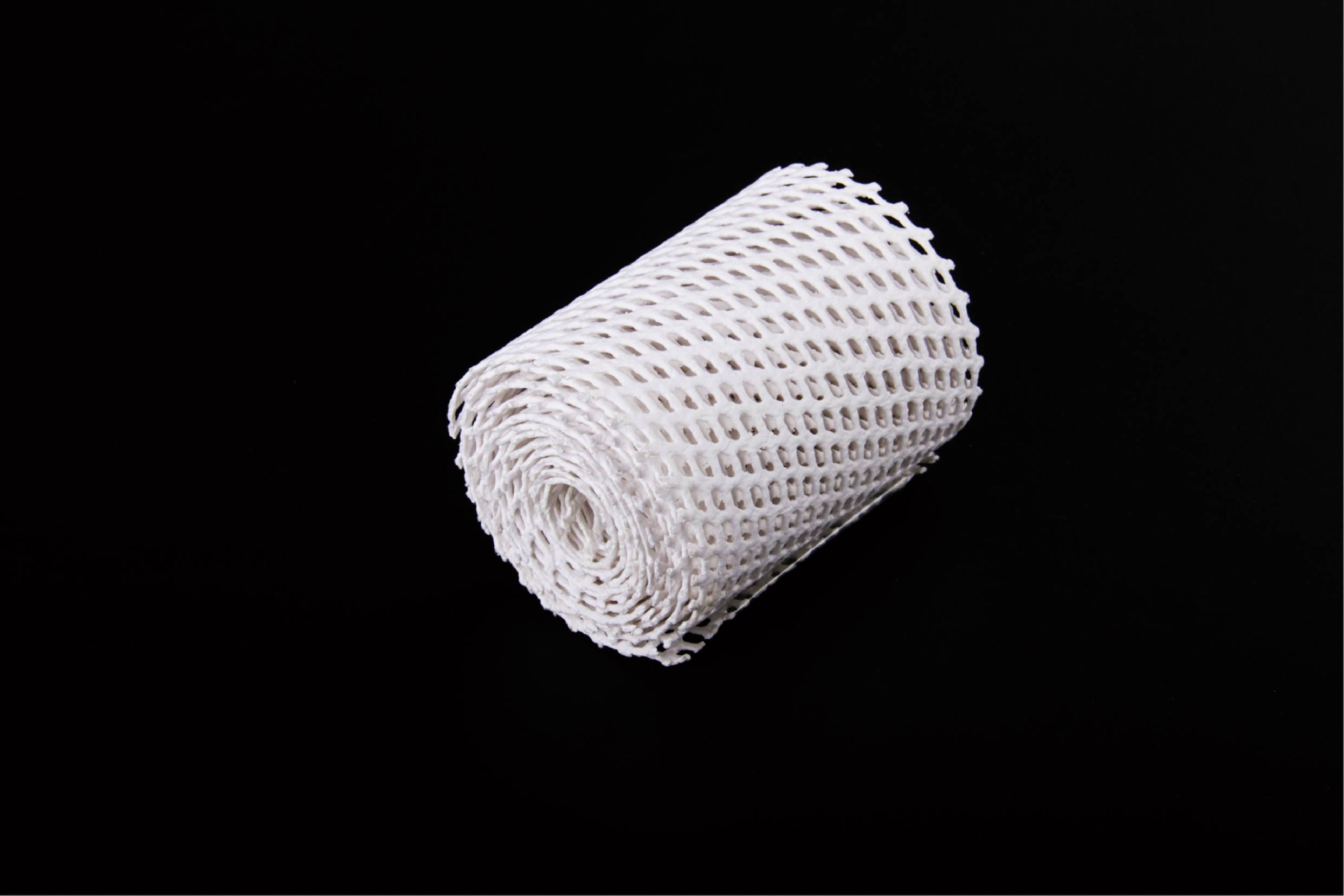 Eine weiße, gerollte elastische Netzbinde auf schwarzem Hintergrund.
