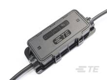 Ein schwarzer Adapter mit dem Logo 'TE' ist an einem Kabel befestigt. Der Adapter hat mehrere Symbole auf der Oberseite.