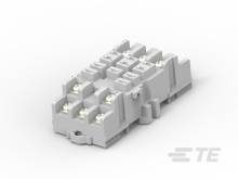 Ein graues elektronisches Bauteil mit mehreren Anschlüssen und strukturierten Oberflächen, auf einer neutralen Oberfläche liegend.