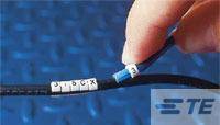 Eine Hand hält ein dünnes schwarzes Kabel mit einem blauen Streifen. Auf dem Kabel befinden sich weiße Plastikringe mit den Buchstaben 'J', 'B', 'C', 'X'.