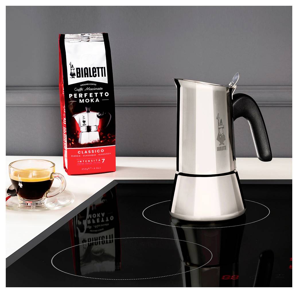 Ein Espressokocher auf einem Induktionsherd, daneben eine Tasse Espresso und eine Packung mit der Aufschrift 