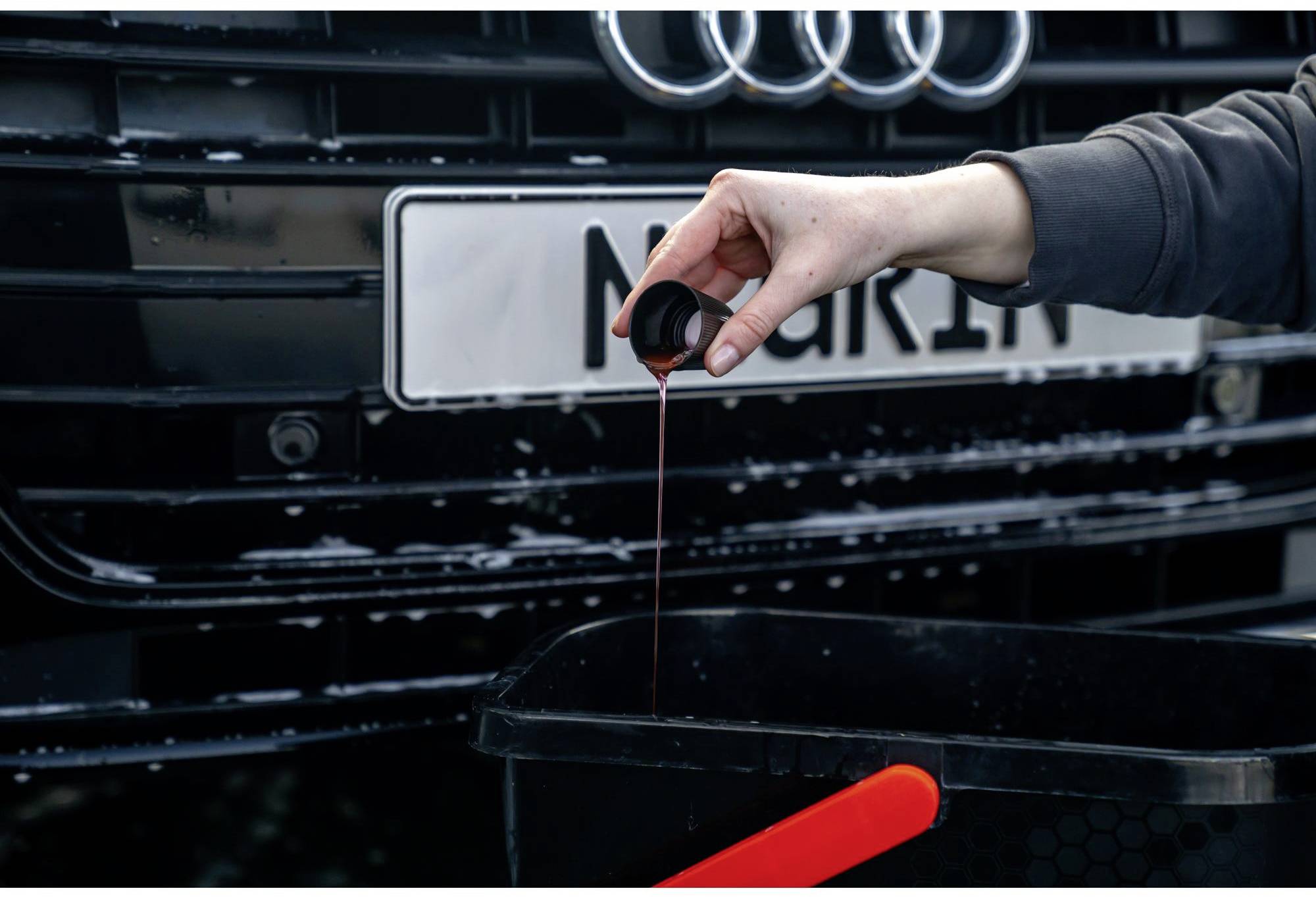 Ein Mensch füllt rote Flüssigkeit aus einem Behälter in einen schwarzen Auffangbehälter vor einem Auto.