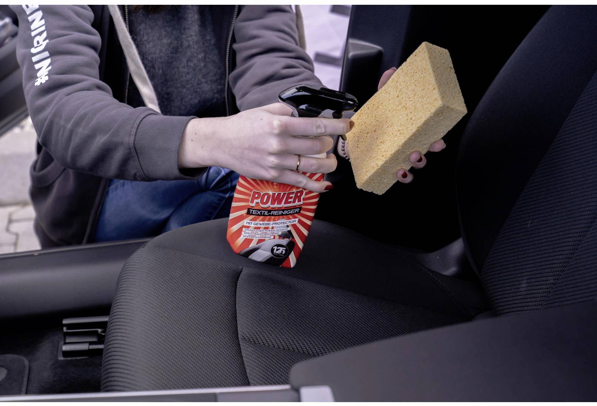 Eine Person reinigt mit einem Reinigungsmittel und einem Schwamm den Autositz.