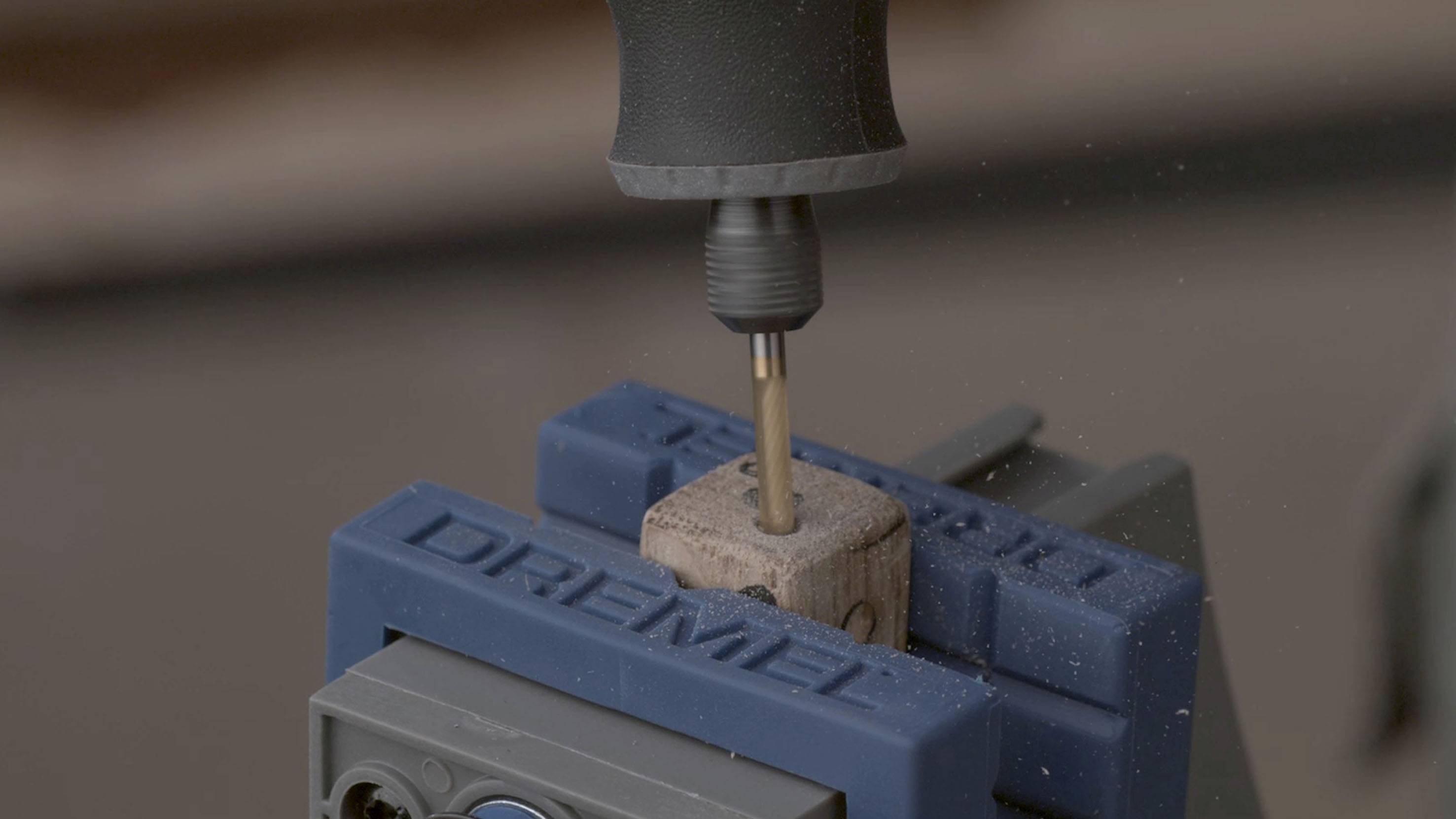 Holzstück in Blauem Schraubstock mit Dremel-Werkzeug eingespannt, während ein Bohrer ein Loch bohrt.