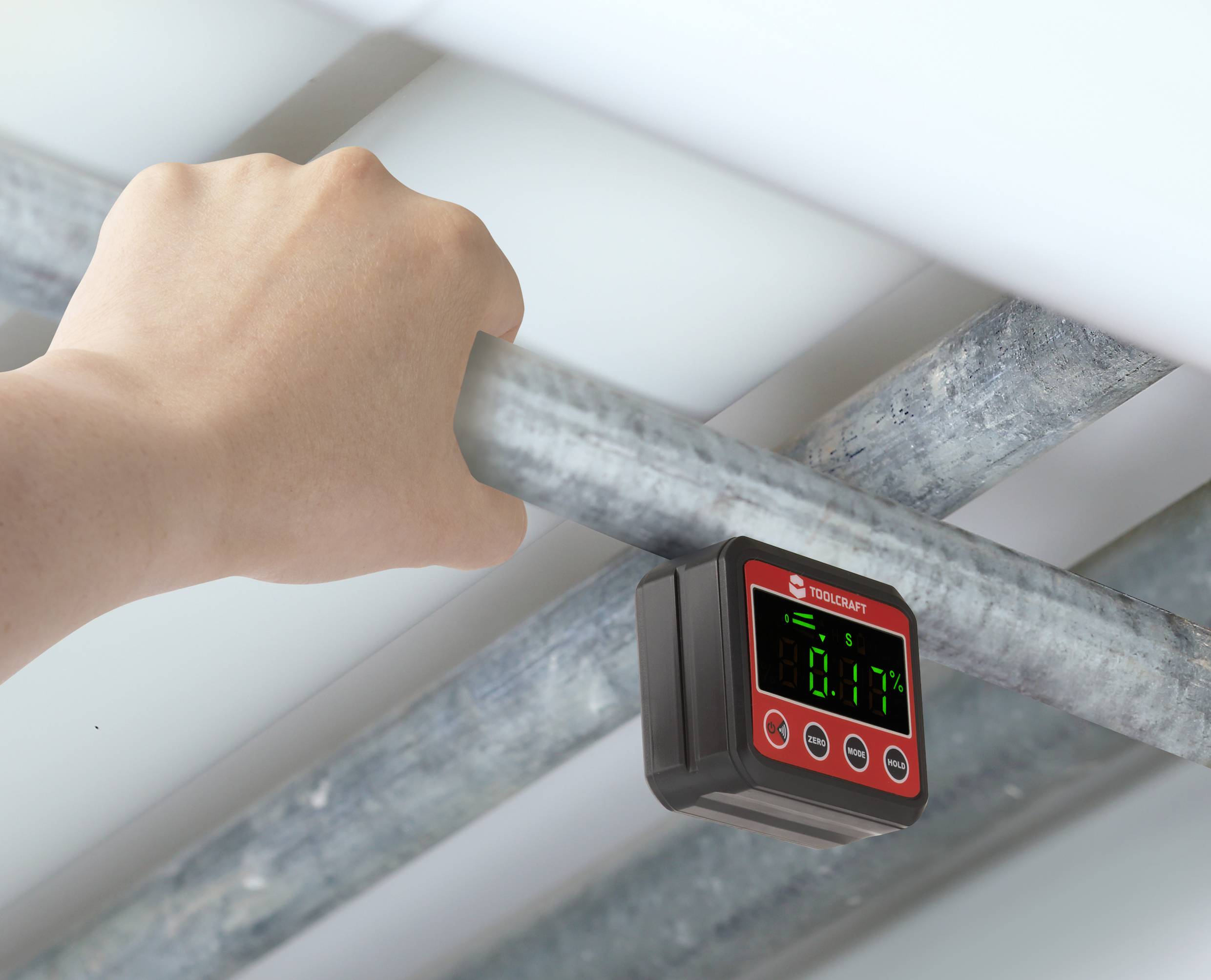 Hand hält Metallrohr, unter dem ein digitales Messgerät befestigt ist. Gerät zeigt Messwert '80.1' auf grünem Display an.