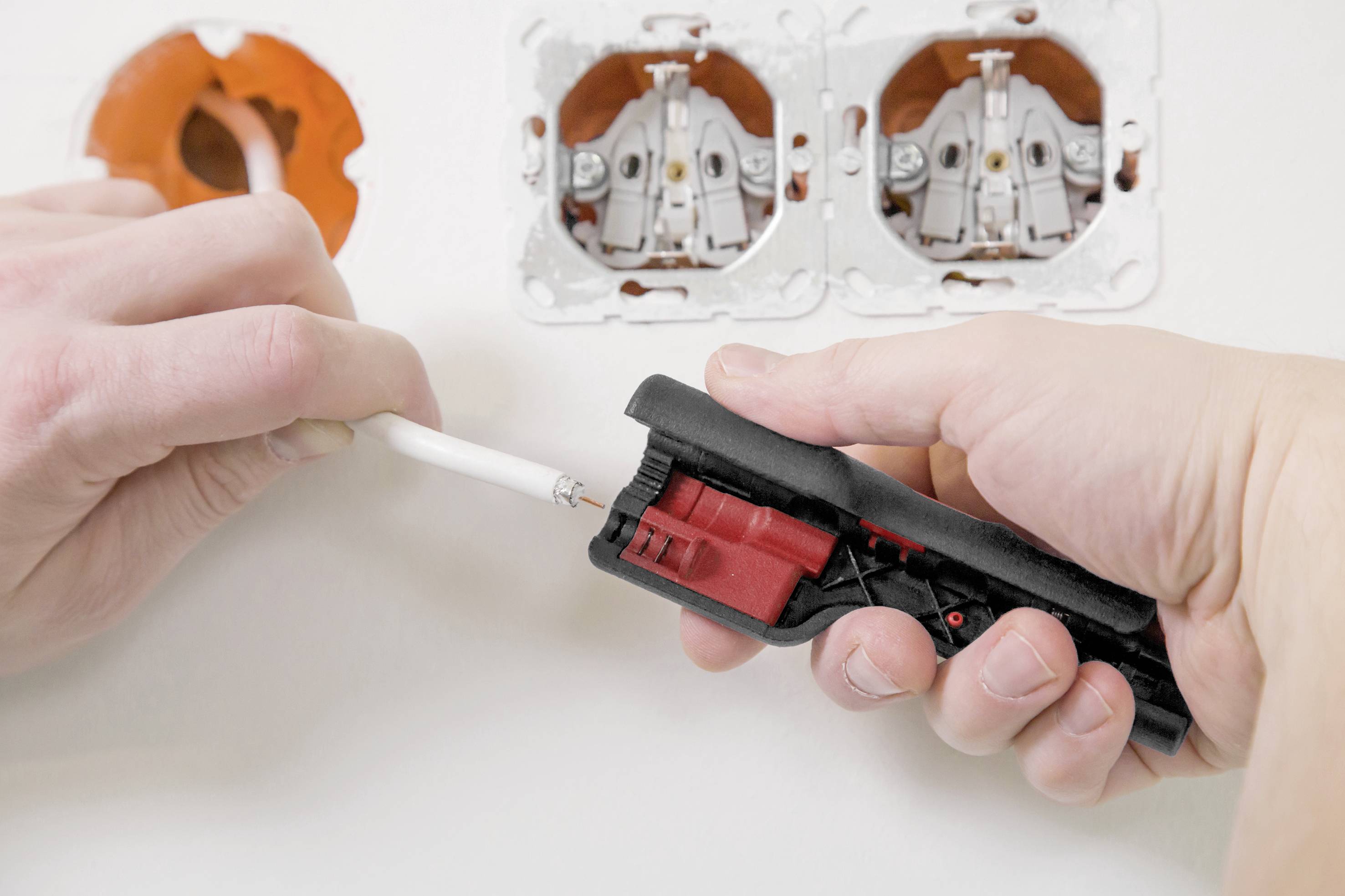Person schneidet mit einer Kabelschere ein elektrisches Kabel vor einer offenen Steckdose.