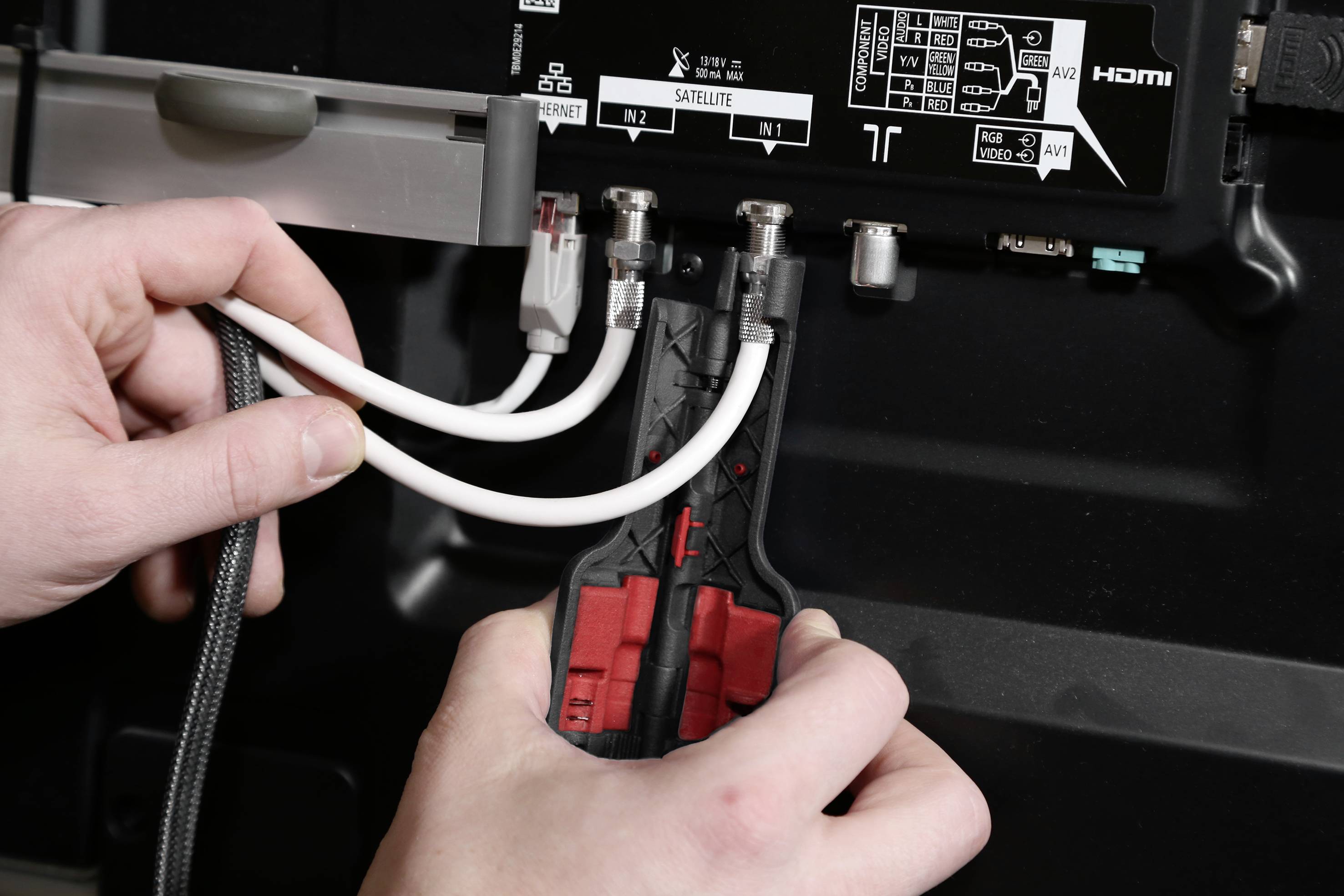 Jemand verbindet Kabel mit der Rückseite eines Fernsehers; HDMI- und andere Anschlüsse sind sichtbar.