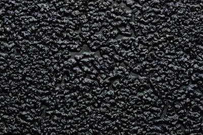 Raue schwarze Texturoberfläche mit unregelmäßigen Erhebungen und Vertiefungen.