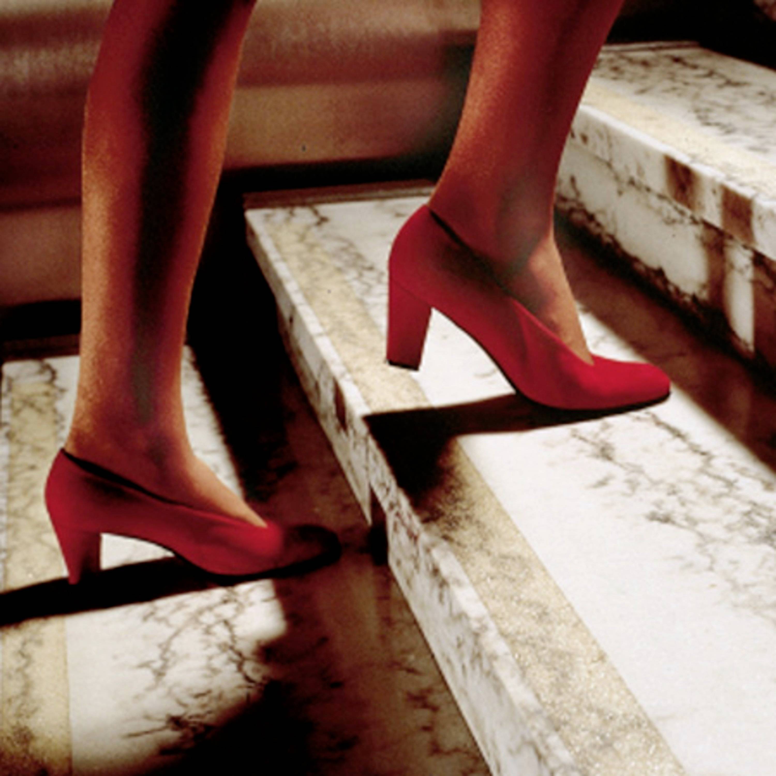 Eine Person geht eine Treppe hinauf, die rote Schuhe trägt. Die Treppe hat eine Marmorstufe.