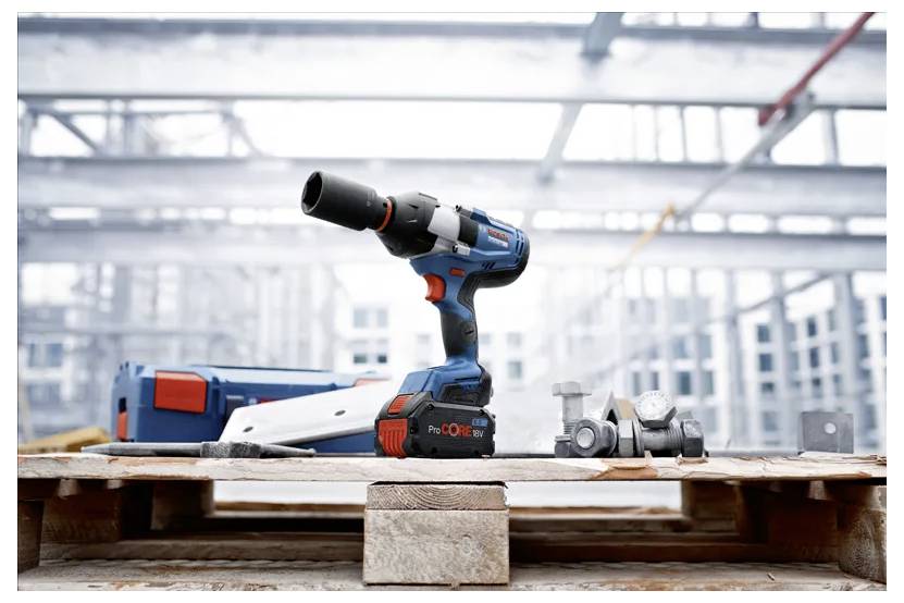 Eine kabellose Bohrmaschine mit Bohrern, die auf einer Holzpalette in einer industriellen Bauumgebung mit Stahlrahmenwerk im Hintergrund platziert ist.