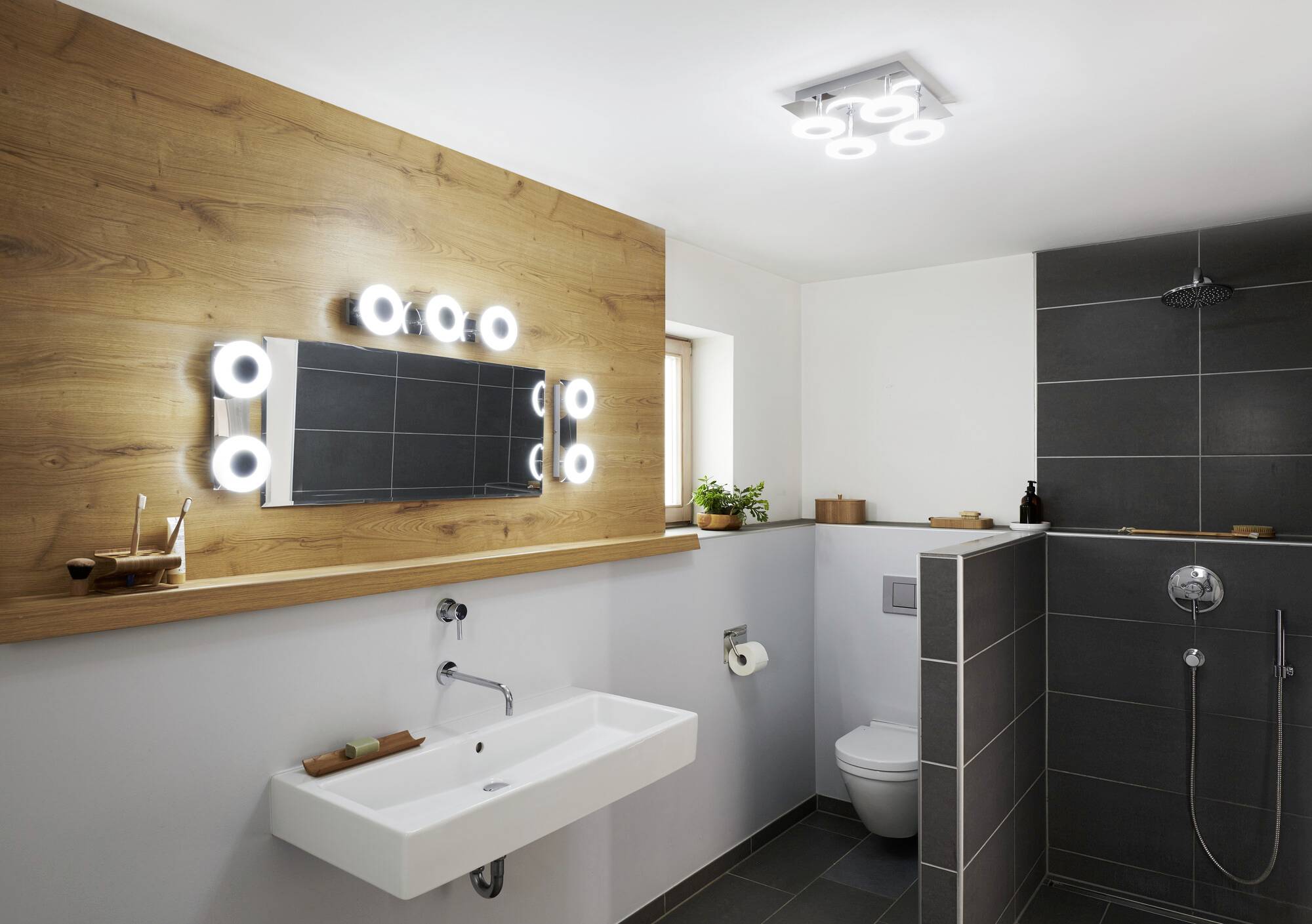 Modernes Badezimmer mit beleuchtetem Spiegel, Waschbecken, Toilette und ebenerdiger Dusche. Dezente Dekoration und Pflanzen.