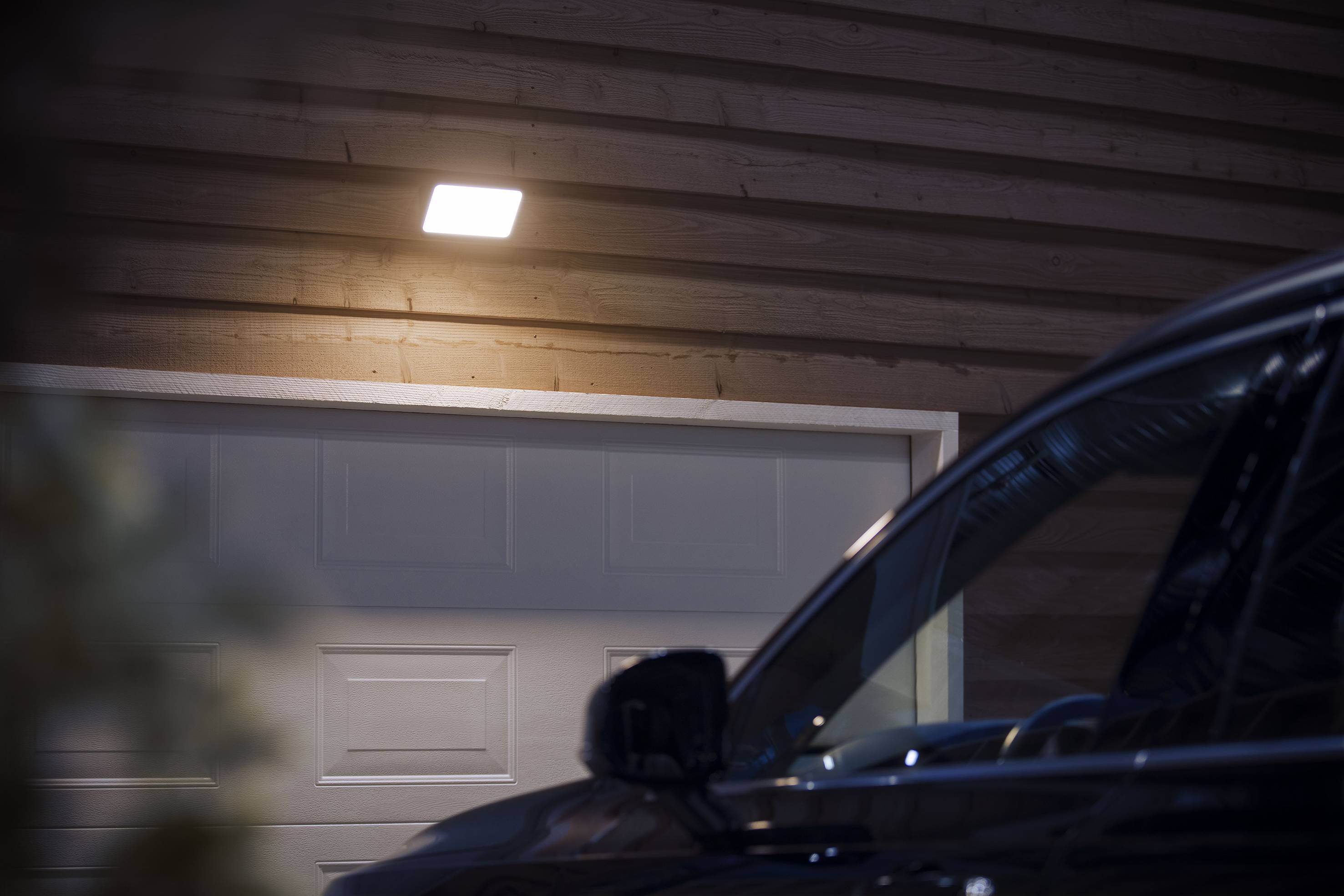 Auto parkt vor einer geschlossenen Garagentür, beleuchtet von einer Außenlampe.