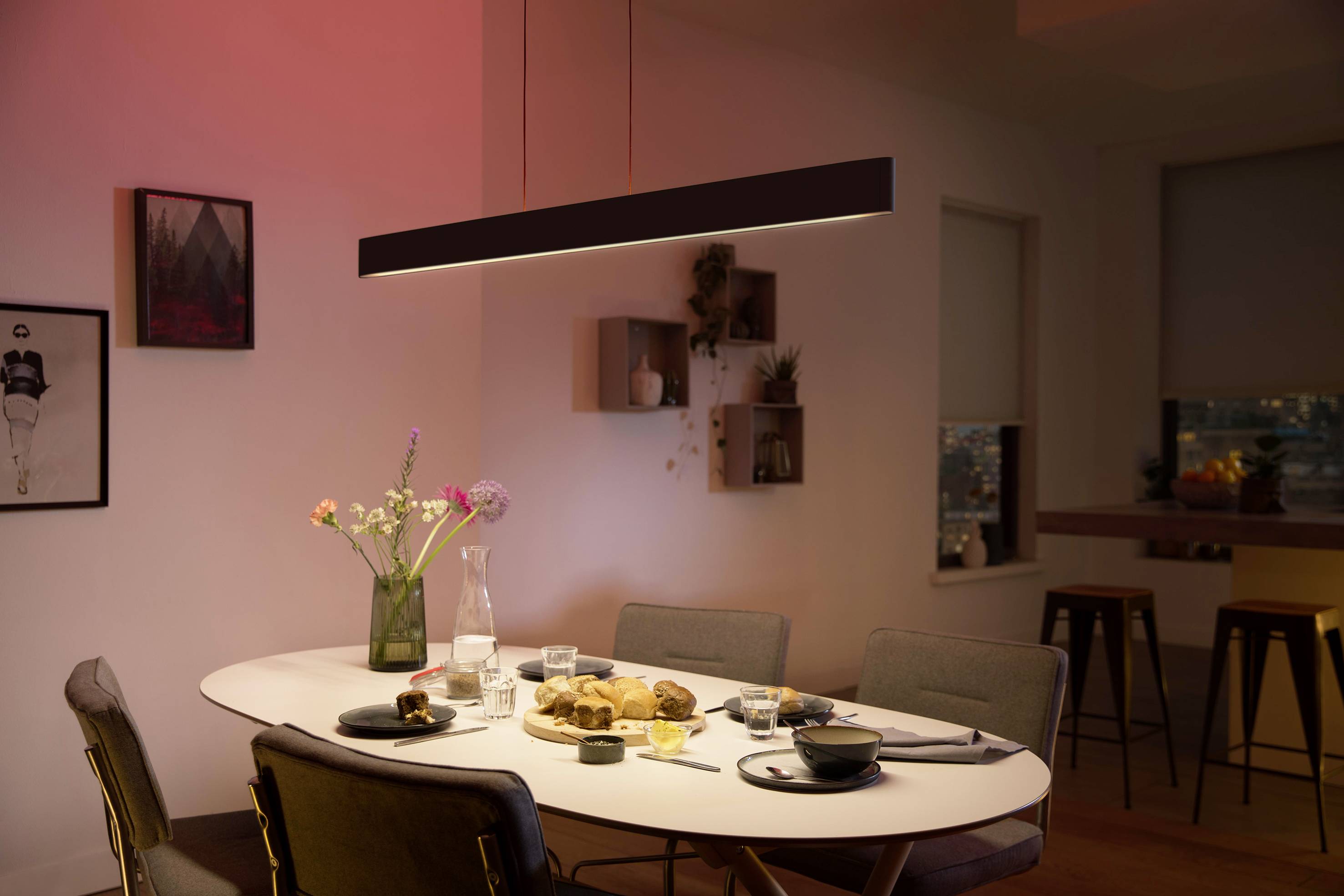 Esszimmer mit Tisch, Stühlen und gedeckter Tafel. Eine Hängelampe beleuchtet den Raum mit rotem Licht. Wanddekorationen im Hintergrund.