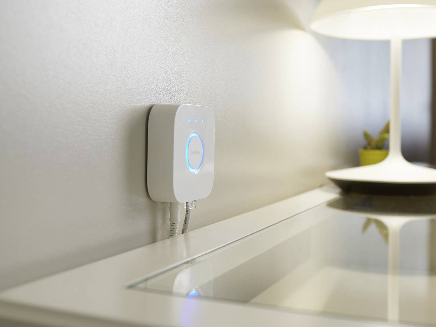 Steuergerät für Smart-Home-Beleuchtung an der Wand, daneben eine eingeschaltete Tischlampe auf einem Schreibtisch.