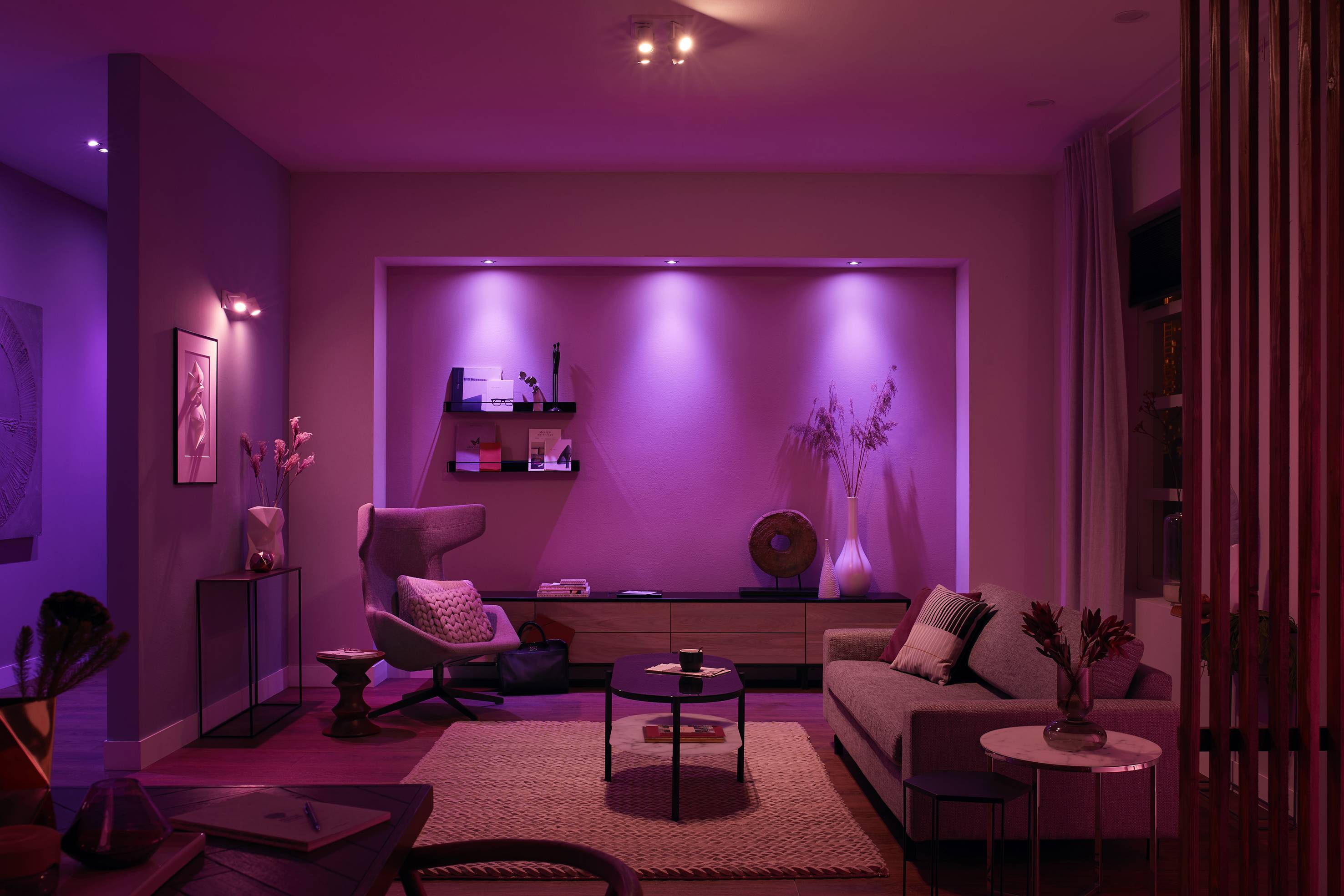 Ein modernes Wohnzimmer mit gedämpfter lila Beleuchtung. Bequeme Sitzecke mit Sessel, Sofa, Regalen und minimalistischen Dekorationen.