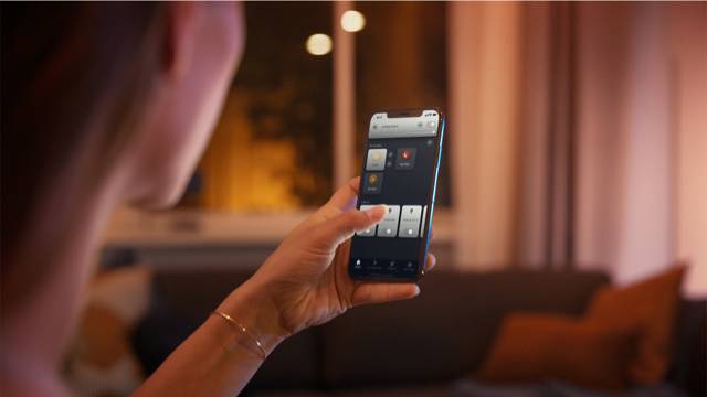 Eine Person benutzt ein Smartphone, um smartes Beleuchtungssystem in einem gemütlichen Wohnzimmer zu steuern.
