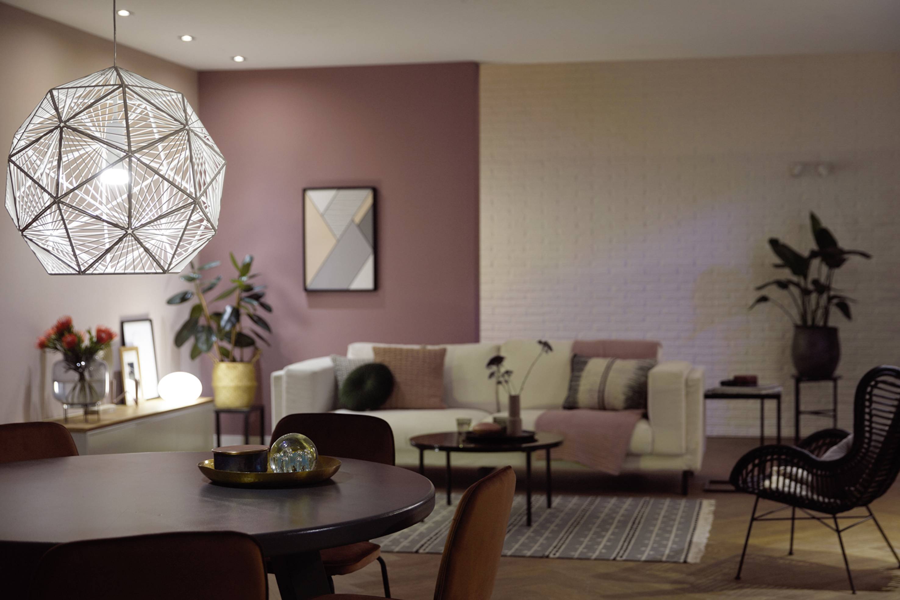 Modernes Wohnzimmer mit geometrischen Formen und stimmungsvoller Beleuchtung. Ein Sofa mit Kissen, ein runder Tisch und Pflanzen sind sichtbar.