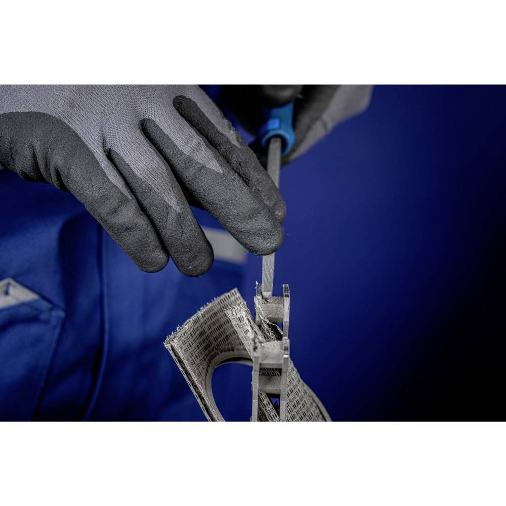 Eine Person in blauer Arbeitskleidung schneidet mit gepolsterten Handschuhen Metallstücke mit einem Werkzeug.
