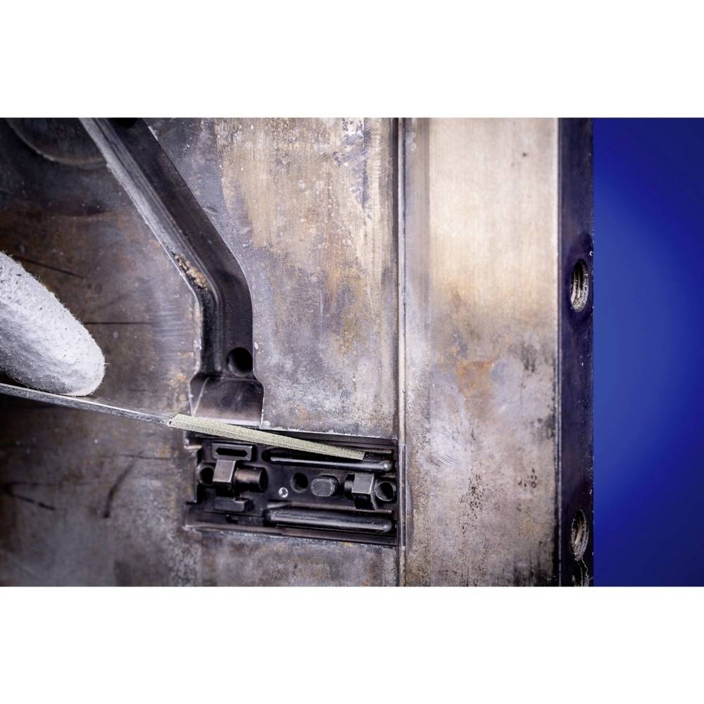 Nahaufnahme eines Metallwerkszeugs, das ein dünnes, grünes Materialstück schneidet. Der Hintergrund ist blau.