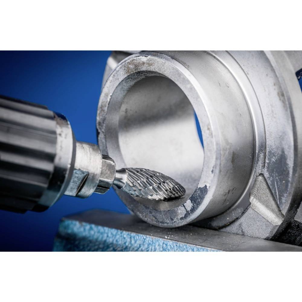 Eine Metallbohrmaschine bearbeitet das Innere eines zylindrischen Metallstücks, wobei Späne entstehen. Die Szene zeigt industrielle Fertigung.