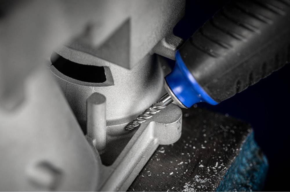 Nahaufnahme einer Bohrmaschine mit blauem Griff, die Metall bearbeitet. Es zeigt die präzise Arbeit des Bohrens oder Fräsens.