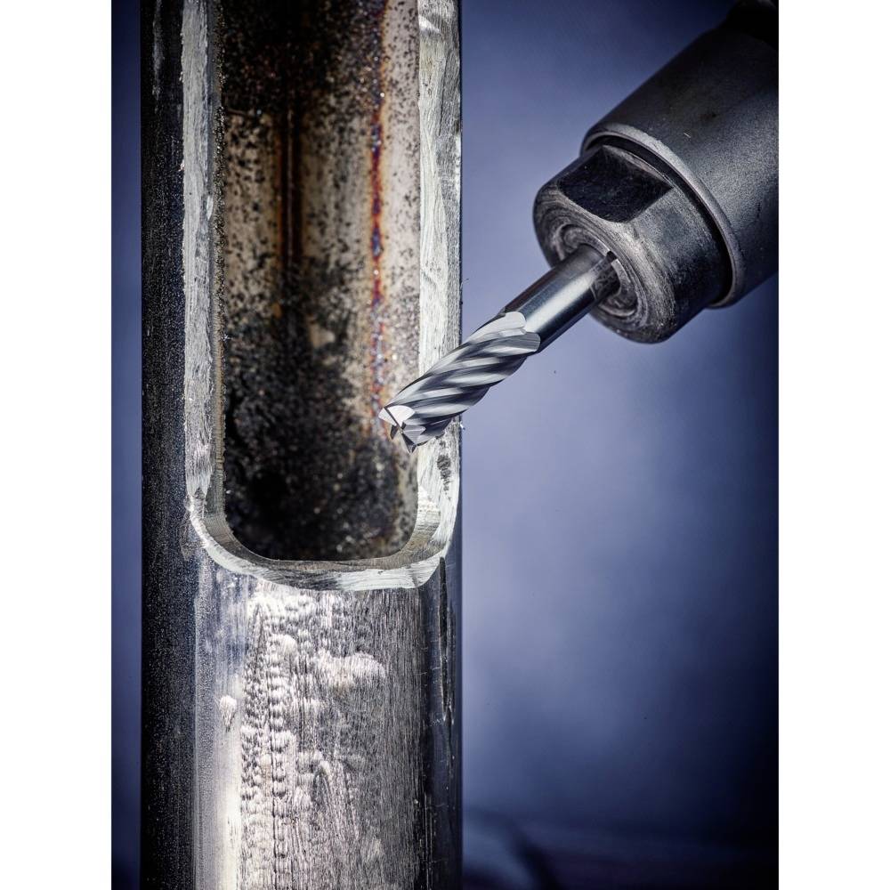 Ein Bohrer bearbeitet ein Metallrohr, erzeugt Späne. Kontrast zwischen poliertem Metall außen und dunkler Oberfläche innen.