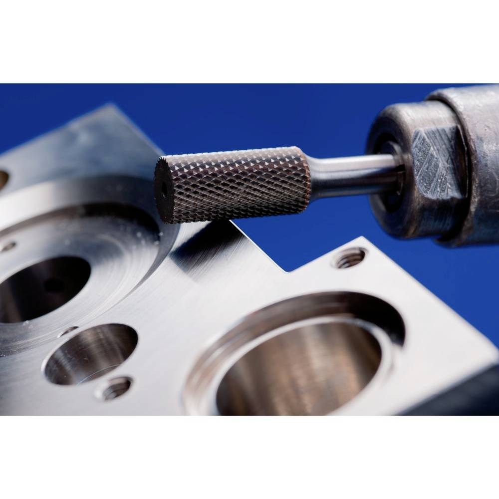 Nahaufnahme eines Metallschleifwerkzeugs, das eine glatte Oberfläche auf einem Metallblock poliert. Der Block hat mehrere kreisförmige Vertiefungen.