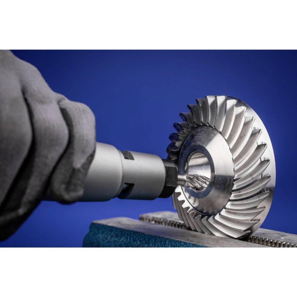 Ein Metallarbeiter schleift einen Turbinenrotor mit einem Elektroschleifwerkzeug. Der Hintergrund ist blau.