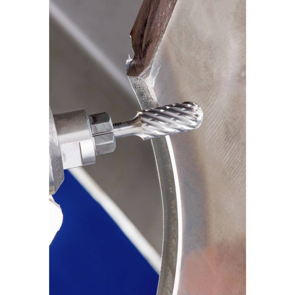 Nahaufnahme eines Metallfräsers beim Bearbeiten einer Metallkante. Der Fräser hat eine zylindrische Form mit spiralförmigen Kerben.