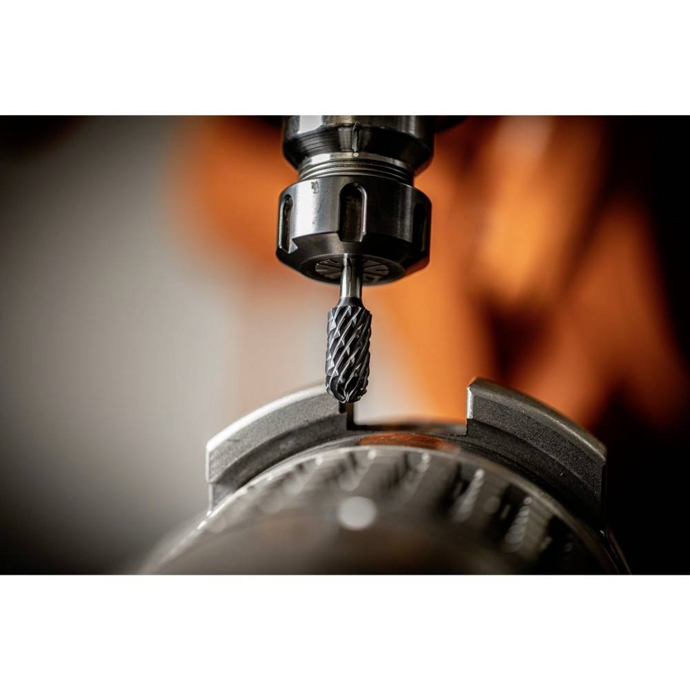 Eine Fräsmaschine bearbeitet ein Metallzahnrad mit präzisem Werkzeug vor einem verschwommenen, orangenen Hintergrund.