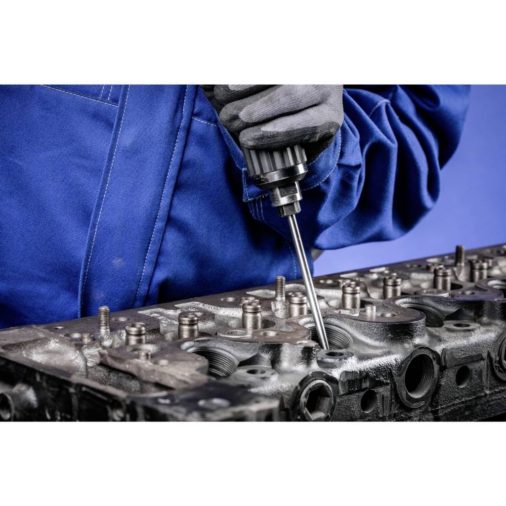 Eine Person in blauer Arbeitskleidung arbeitet an einem Zylinderkopf mit einem Elektrowerkzeug.