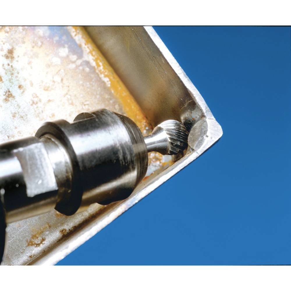 Ein Metallfräser bearbeitet die Innenkante eines rostigen Metallstücks vor blauem Hintergrund.