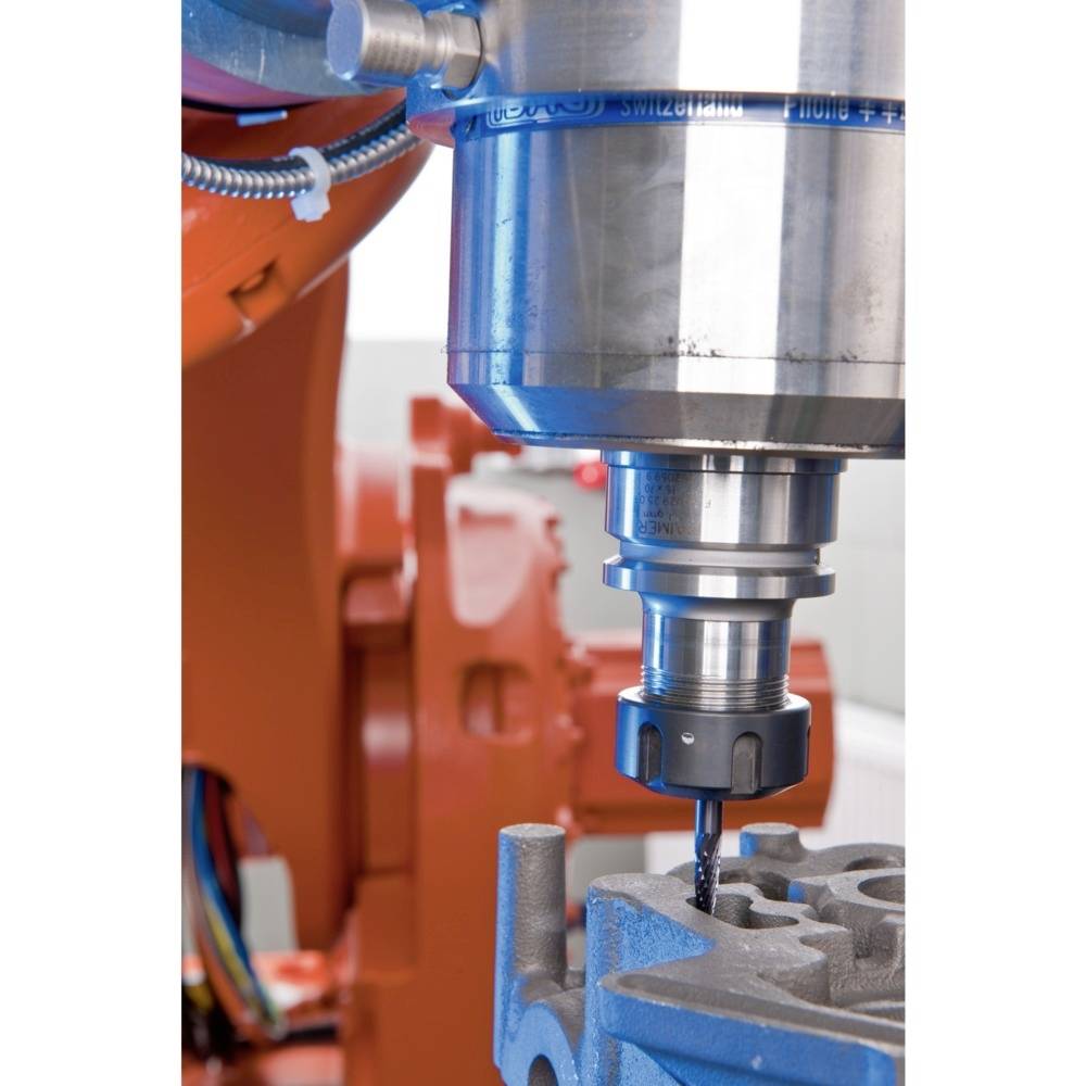 Eine CNC-Maschine bearbeitet präzise ein Metallwerkstück. Der Bohrer gräbt sich in das Material. Im Hintergrund sind industrielle Teile sichtbar.