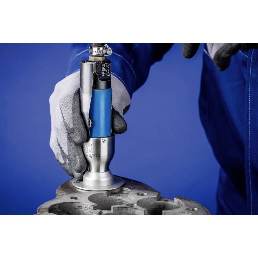 Eine Person in blauer Arbeitskleidung und grauen Handschuhen hält ein Werkzeug an einem Metallteil. Das Werkzeug ist teilweise blau.