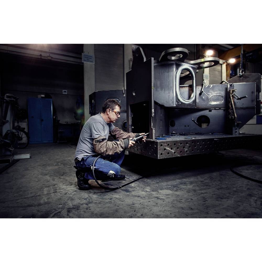 Ein Mann arbeitet in einer Werkstatt an einer großen Metallkonstruktion. Er trägt Schutzkleidung und scheint konzentriert zu sein.