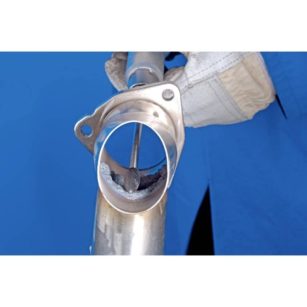 Eine Person in blauer Arbeitskleidung bearbeitet das Innere eines metallischen Rohrs mit einem Werkzeug. Technische Arbeit in Fokus.