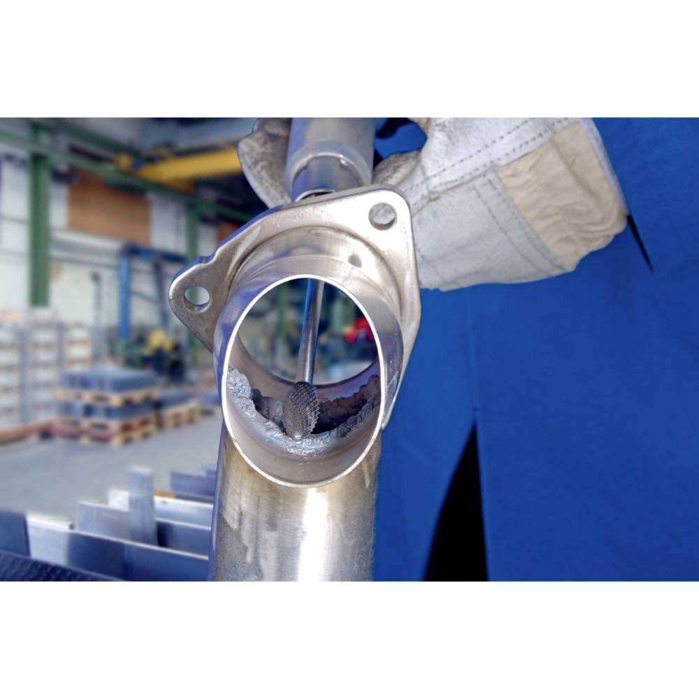 Nahaufnahme von einer Person, die mit Schutzhandschuhen ein rundes Metallteil inspiziert, im Hintergrund unscharf eine Werkstatt.