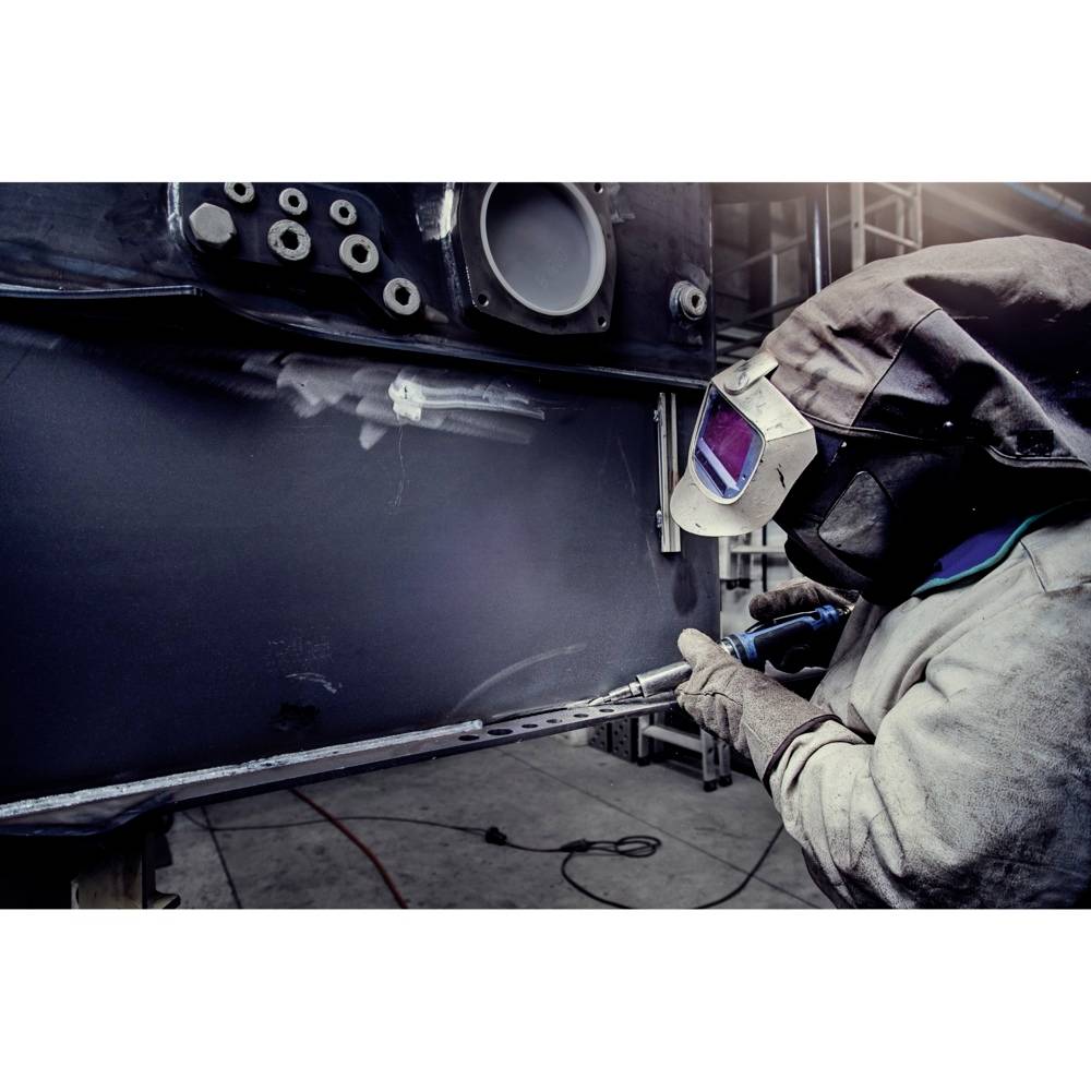 Ein Arbeiter in Schutzkleidung schweißt mit einem Lichtbogen an einem Metallstück. Die Umgebung wirkt industriell und gut beleuchtet.