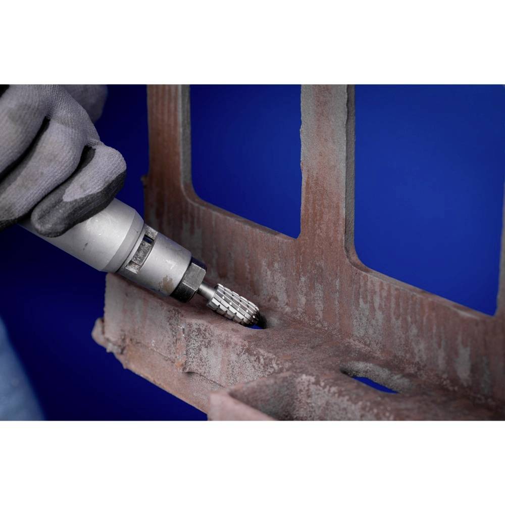 Eine behandschuhte Hand hält ein Werkzeug mit Schleifkopf, das Rost von einer Metalloberfläche entfernt. Hintergrund in Blau.