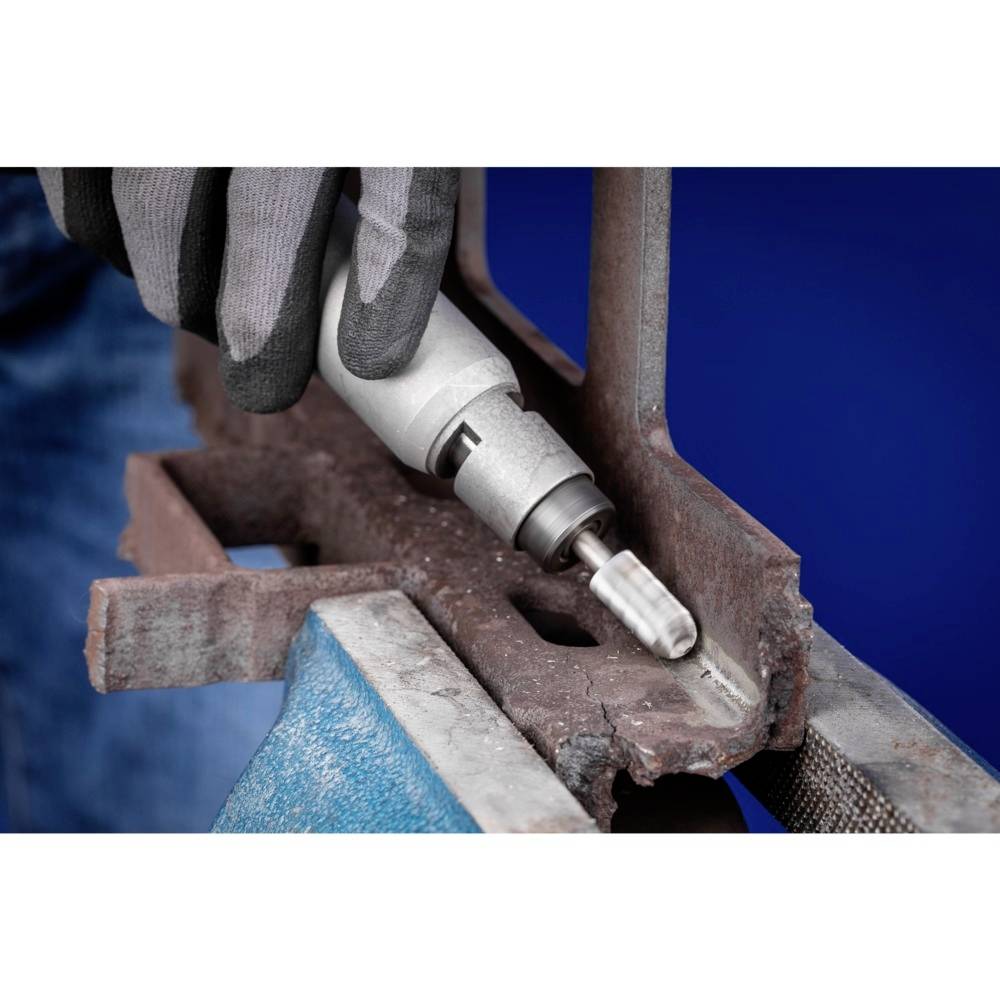 Eine Person bearbeitet ein rostiges Metallstück mit einem Handwerkzeug. Sie trägt Handschuhe. Der Hintergrund ist unscharf blau.