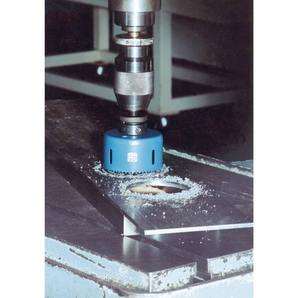 Eine blaue Kreissäge bohrt ein Loch in eine Metallplatte. Metallspäne sind um das Loch verteilt. Die Maschine arbeitet präzise.