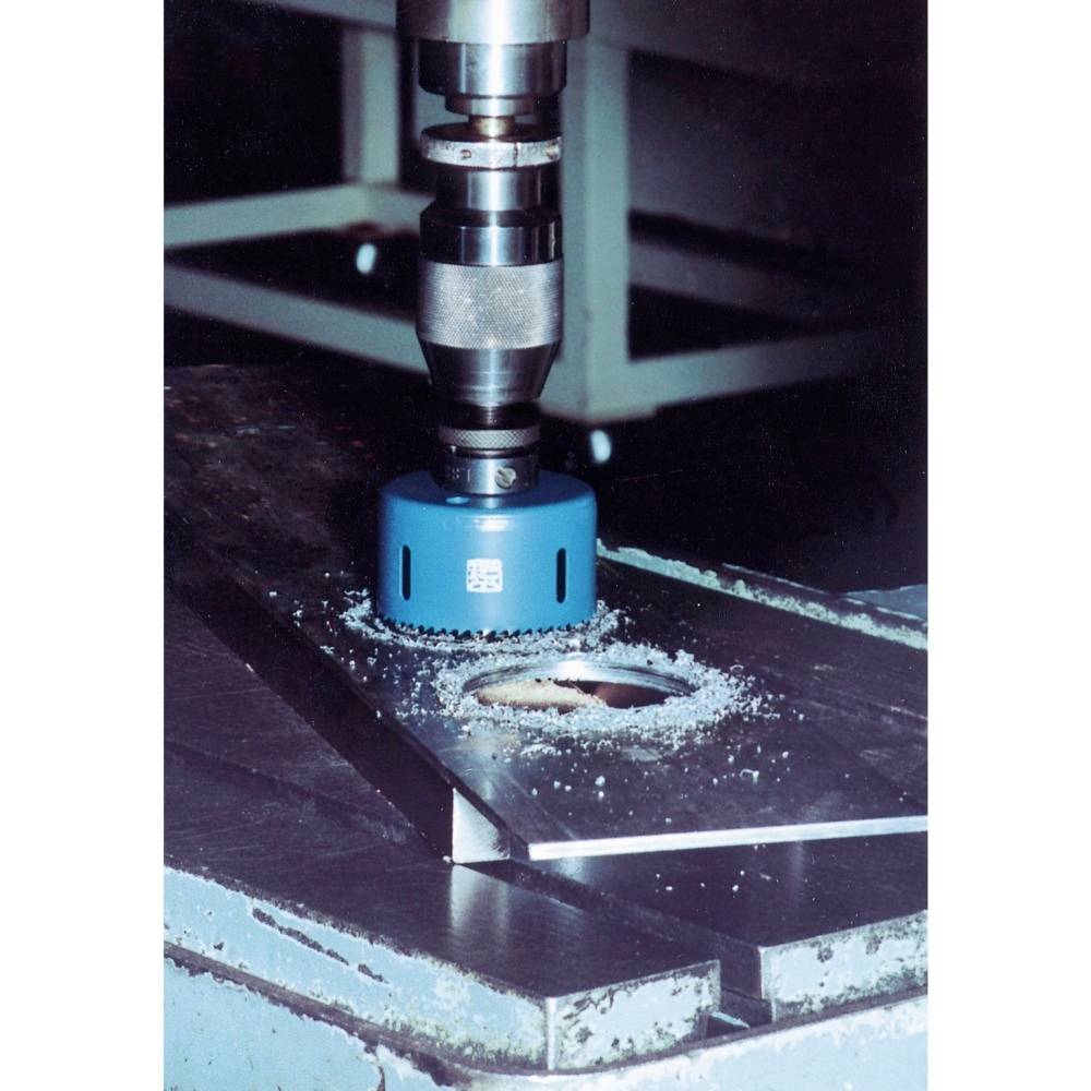 Eine blaue Bohrkrone auf einer Metallplatte, die ein kreisförmiges Loch bohrt. Metallspäne sind um das Loch verteilt.