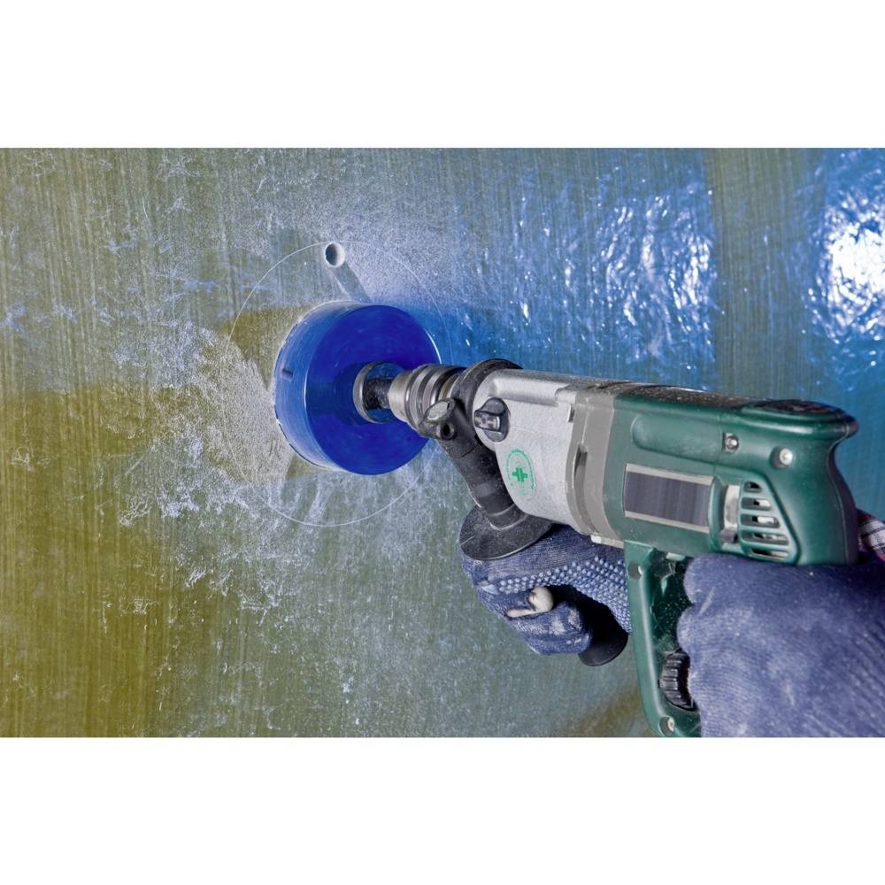 Eine Person trägt Sicherheitshandschuhe und bohrt mit einer elektrischen Bohrmaschine ein rundes Loch in eine glatte, blaue Oberfläche.