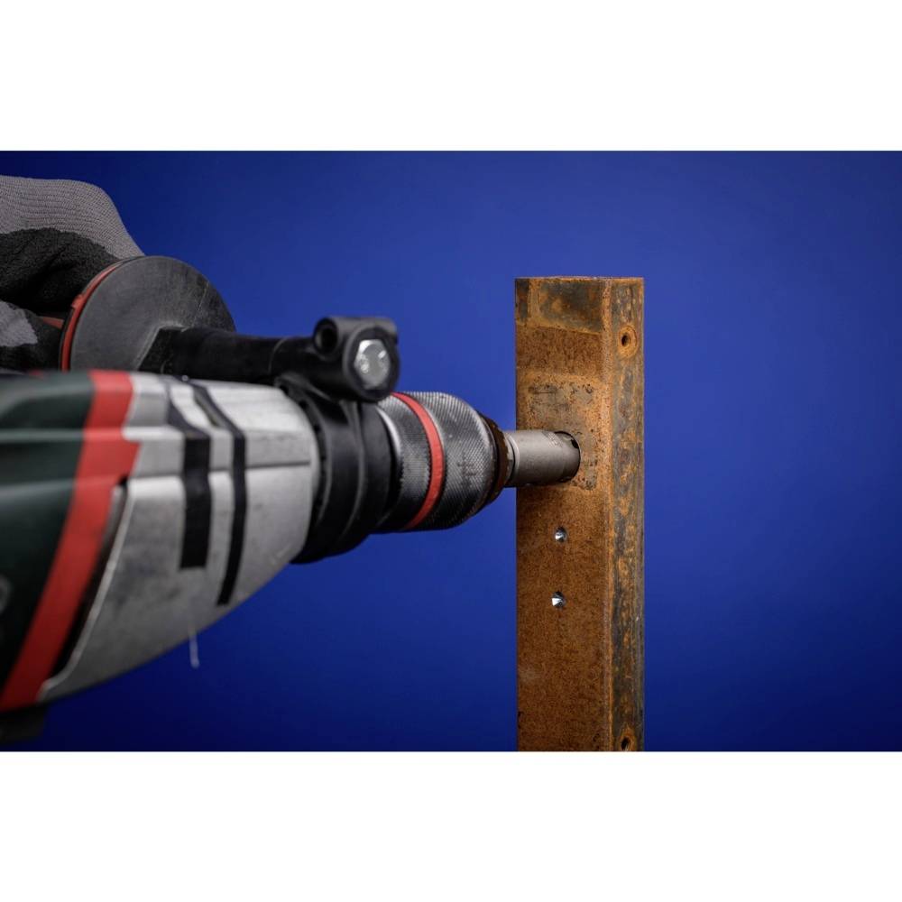 Eine Bohrmaschine durchbohrt ein rostiges Metallstück vor einem blauen Hintergrund.