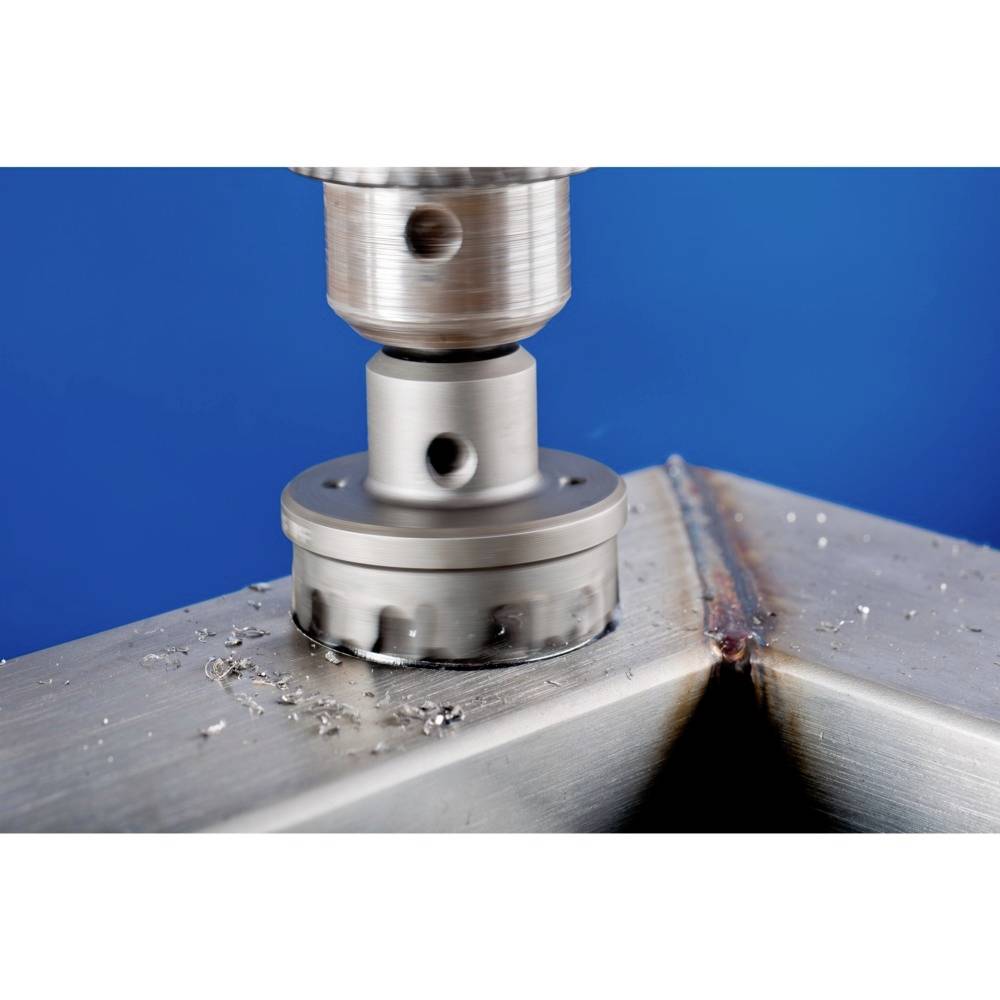 Eine Metallbohrmaschine arbeitet an einem Metallstück, das Späne erzeugt. Hintergrund ist blau.