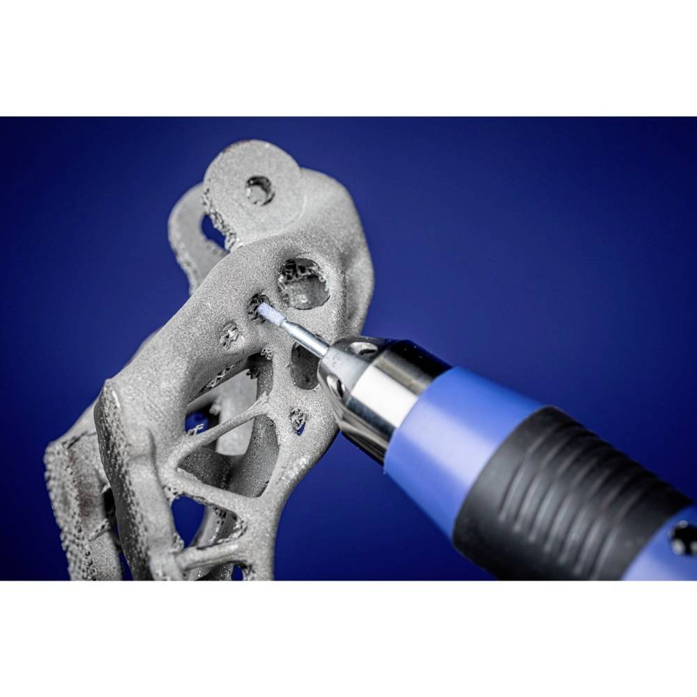 Ein Bohrer arbeitet an einem komplex strukturierten Metallobjekt vor blauem Hintergrund. Technik oder Fertigung im Fokus.